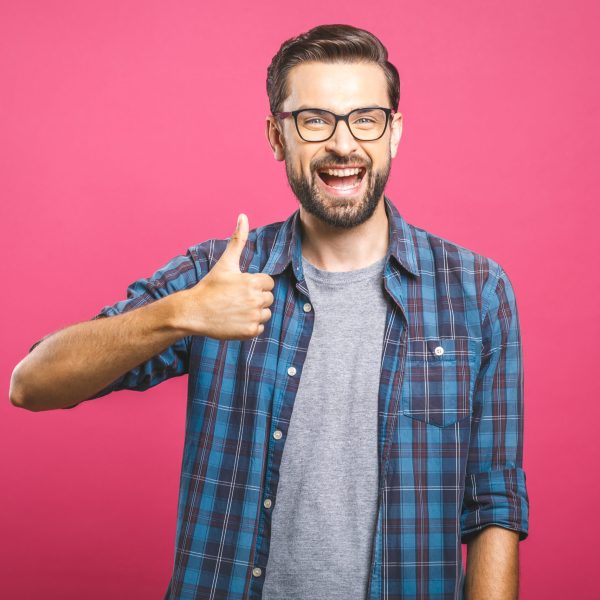 Portrait of young man in glasses showing thumbs up isolated over pink background